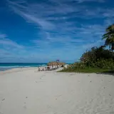 Traumhafter Strand in Kuba Varadero mit Palmen, Sonnenschirmen und dem türkisfarbenen Meer unter blauem Himmel.