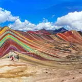 Regenbogenberg in Peru im September. Wanderer bestaunen die bunten Mineralstreifen der Berge unter blauem Himmel.