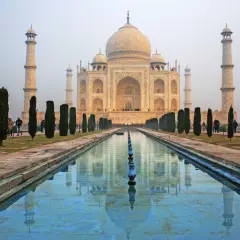 Das Taj Mahal, eine Moschee, spiegelt sich im Wasser. Besucher spazieren durch den Garten.