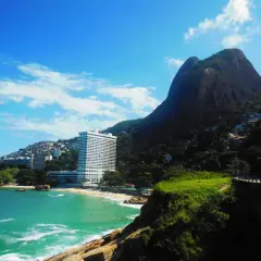 Traumhafter Blick auf Leblon, Rio de Janeiro: Türkisfarbenes Meer, ein Strand mit Palmen und das imposante Sheraton Hotel vor einem Berg.