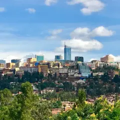 Blick auf die Skyline von Ruanda, Kigali, mit vielen Gebäuden auf grünen Hügeln unter einem blauen Himmel mit Wolken.