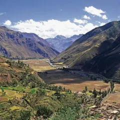 Weites Tal in den Peru Anden, mit terrassierten Feldern, einem Fluss und einem Dorf.
