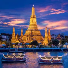 Wat Arun im Abendlicht, ein absolutes Bangkok Must-See. Boote auf dem Fluss vor dem beleuchteten Tempel.