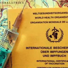 Gelber Impfpass der WHO liegt auf einer Karte von Zentralafrika. Spritze daneben. Wichtig für Reisen nach Malaysia, Impfungen sind oft Pflicht.
