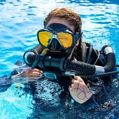 Taucherin mit gelber Maske und Atemregler im klaren Wasser, bereit für das Tauchen auf Bali.