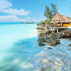 Traumhaftes Sansibar Wetter im Mai: Türkises Meer trifft auf felsige Küste mit Strohdach-Bungalows. Perfekt für einen entspannten Urlaub.