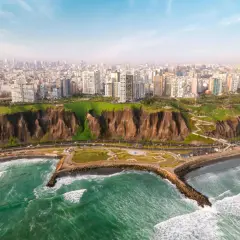 Blick auf die Küste von Lima, wo grüne Hügel auf das Meer treffen. Hochhäuser säumen die Stadt, während die lima einwohner die Küstenpromenade genießen.