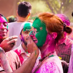 Bunte Gesichter beim Farbenfest in Indien. Menschen lachen und bewerfen sich mit Pulver.