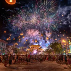 Feuerwerk und Himmelslaternen erleuchten die Nacht beim Thailand Neujahr. Eine Menschenmenge feiert unter dem farbenprächtigen Himmel.