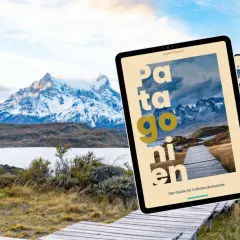 Ein Tablet mit dem Titel "Patagonien" liegt vor einer atemberaubenden Berglandschaft. Der Reiseführer ist die neue Version 25/26.