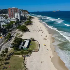 Blick auf den Strand von Barra da Tijuca mit Wellen, Palmen und Gebäuden.