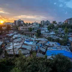 Sonnenuntergang über Addis Abeba. Dächer aus Wellblech und Planen prägen das Bild, während im Hintergrund moderne Gebäude emporragen. Die **Addis Abeba Sicherheit** ist ein komplexes Thema, das sich in diesem Kontrast widerspiegelt.
