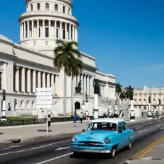 Blauer Oldtimer fährt am Kapitol vorbei. Kuba Sicherheit ist spürbar, Palmen säumen die Straße.