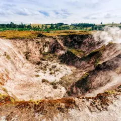 Dampf steigt aus einem Krater in Taupō, Neuseeland. Die Erde ist rötlich-weiß, mit grüner Vegetation am Rand.