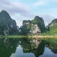 Grüne Berge spiegeln sich im ruhigen Wasser. Ein Tempel schmiegt sich an den Hang. Perfekt für die beste Reisezeit Vietnam.