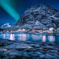 Nordkap Polarlichter tanzen über verschneite Berge und kleine Häuser am Fjord. Ein magischer Anblick!