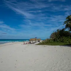 Traumhafter Strand in Kuba Varadero mit Palmen, Sonnenschirmen und dem türkisfarbenen Meer unter blauem Himmel.