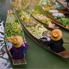 Bunte Boote voller Früchte und Gemüse auf einem **floating market**. Händler mit traditionellen Hüten rudern durch das Wasser.