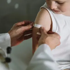Arzt legt Pflaster auf Arm eines Kindes nach Impfung in Thailand. Kindergesundheit ist wichtig.