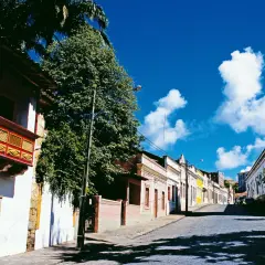 Bunte Kolonialhäuser und Kirche säumen eine Kopfsteinpflasterstraße unter blauem Himmel.