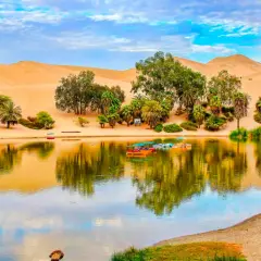 Oase Huacachina bei Ica, Peru, mit Sanddünen, Palmen und einem See voller bunter Boote.