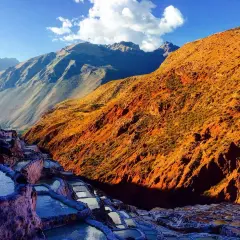 Terrassierte Salinen von Maras, Peru, im warmen Licht der untergehenden Sonne. Die Berge im Hintergrund sind in Schatten getaucht.