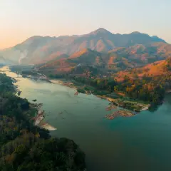 Sonnenuntergang über dem Mekong Delta. Berge, Wälder und ein breiter Fluss mit kleinen Booten.
