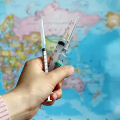 Hand hält Spritzen vor Weltkarte. Gelbfieberimpfung ist für Kap Verde Pflicht.