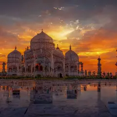 Das Taj Mahal spiegelt sich im Wasser, während ein dramatischer Sonnenuntergang den Himmel in leuchtenden Orange- und Rottönen färbt.