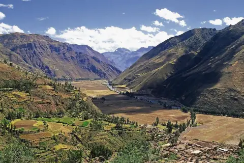 Weites Tal in den Peru Anden, mit terrassierten Feldern, einem Fluss und einem Dorf.