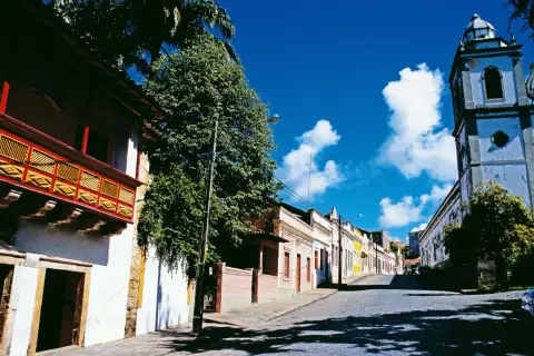 Bunte Kolonialhäuser und Kirche säumen eine Kopfsteinpflasterstraße unter blauem Himmel.