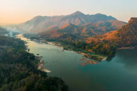 Sonnenuntergang über dem Mekong Delta. Berge, Wälder und ein breiter Fluss mit kleinen Booten.