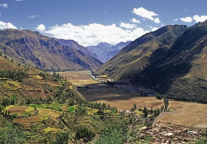 Weites Tal in den Peru Anden, mit terrassierten Feldern, einem Fluss und einem Dorf.