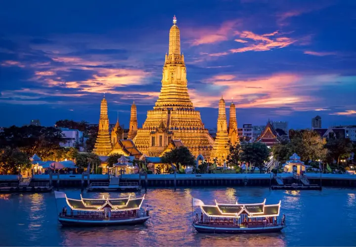 Wat Arun im Abendlicht, ein absolutes Bangkok Must-See. Boote auf dem Fluss vor dem beleuchteten Tempel.
