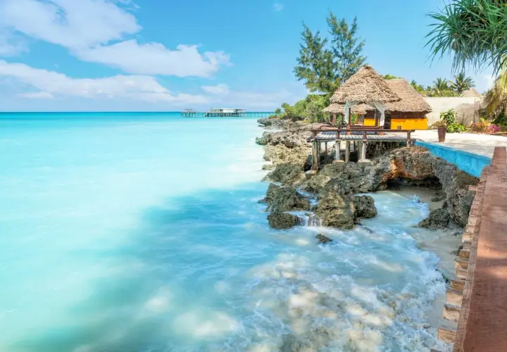 Traumhaftes Sansibar Wetter im Mai: Türkises Meer trifft auf felsige Küste mit Strohdach-Bungalows. Perfekt für einen entspannten Urlaub.