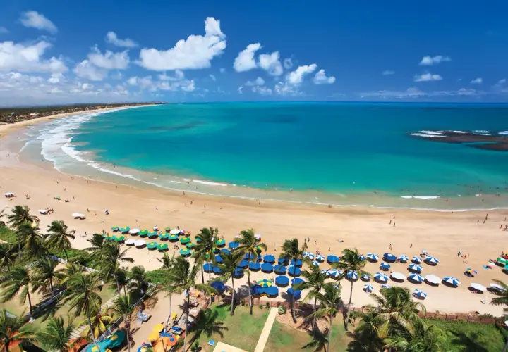 Traumhafter Strand von Porto de Galinhas mit türkisfarbenem Wasser, Palmen und vielen bunten Sonnenschirmen.
