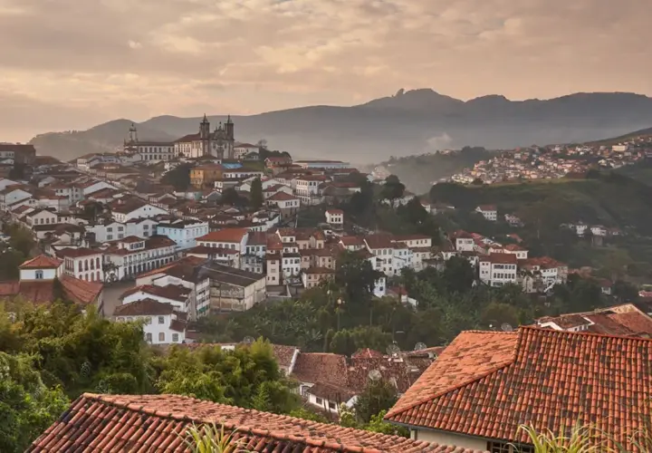 Malerische Hügelstadt Ouro Preto im Morgendunst, mit traditionellen Häusern und einer Kirche im Hintergrund.