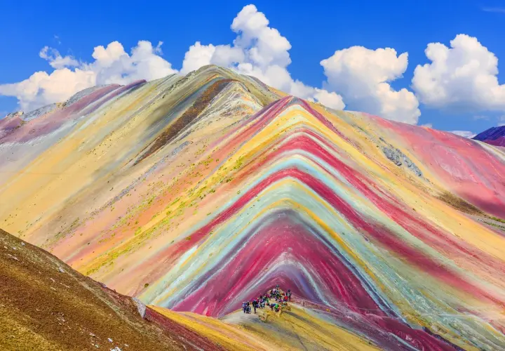 Bunte Streifen ziehen sich über die Berge, wie ein natürlicher Regenbogen. Eine Gruppe Wanderer erkundet diese farbenprächtige Landschaft.