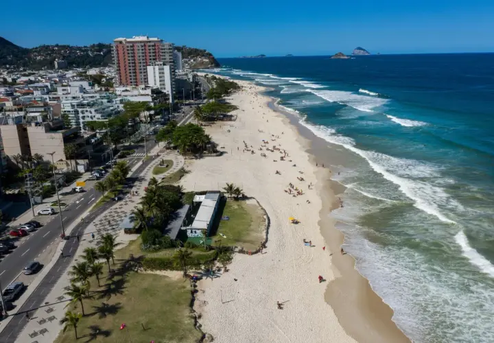 Blick auf den Strand von Barra da Tijuca mit Wellen, Palmen und Gebäuden.
