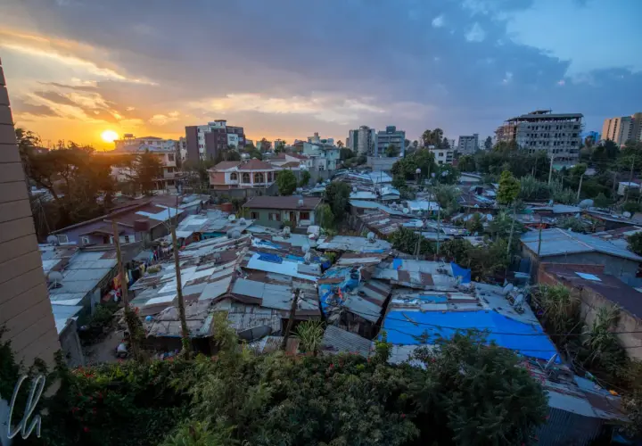 Sonnenuntergang über Addis Abeba. Dächer aus Wellblech und Planen prägen das Bild, während im Hintergrund moderne Gebäude emporragen. Die **Addis Abeba Sicherheit** ist ein komplexes Thema, das sich in diesem Kontrast widerspiegelt.