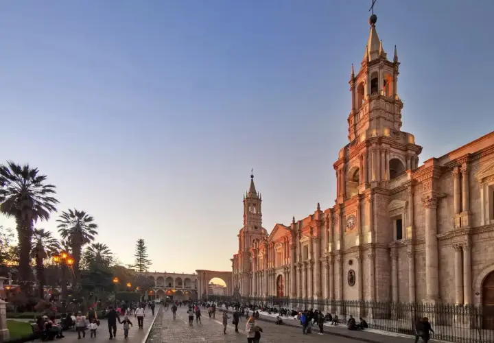 Abendstimmung in Arequipa, Peru. Die Sonne beleuchtet die Kathedrale und die umliegenden Gebäude, während Menschen auf dem Platz spazieren. Die Peru Berge sind in der Ferne zu erahnen.