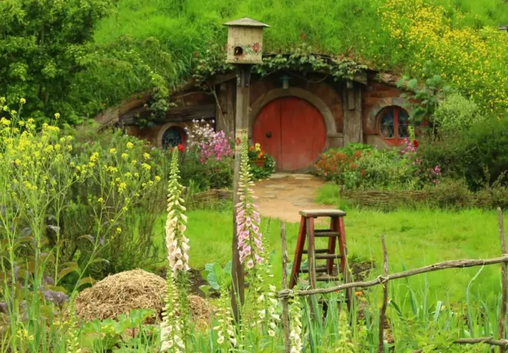 Ein Hobbit-Dorf in Neuseeland, mit einem runden roten Tor, umgeben von üppiger Natur und bunten Blumen.