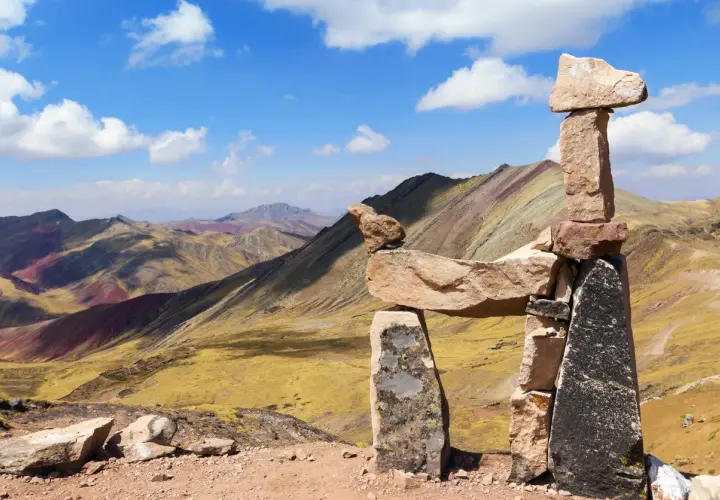 Bunte Berge in Peru, bekannt als Regenbogenberg, mit einer Steinpyramide im Vordergrund.