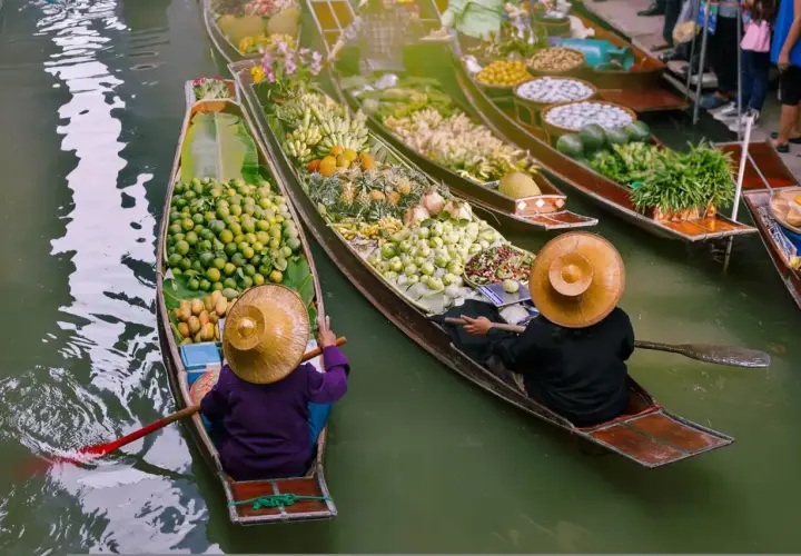 Bunte Boote voller Früchte und Gemüse auf einem **floating market**. Händler mit traditionellen Hüten rudern durch das Wasser.