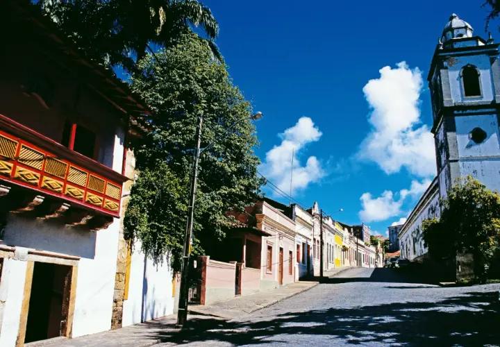 Bunte Kolonialhäuser und Kirche säumen eine Kopfsteinpflasterstraße unter blauem Himmel.