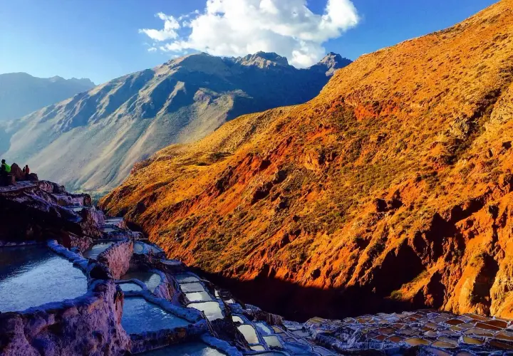 Terrassierte Salinen von Maras, Peru, im warmen Licht der untergehenden Sonne. Die Berge im Hintergrund sind in Schatten getaucht.