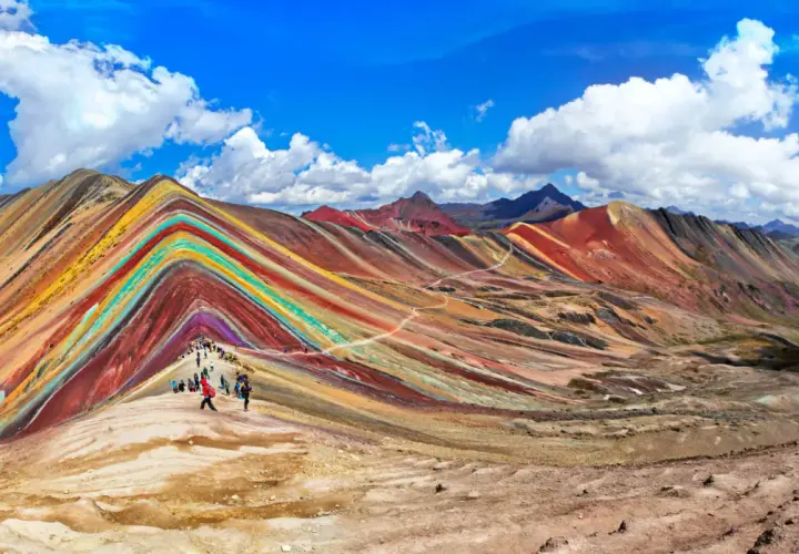 Regenbogenberg in Peru im September. Wanderer bestaunen die bunten Mineralstreifen der Berge unter blauem Himmel.