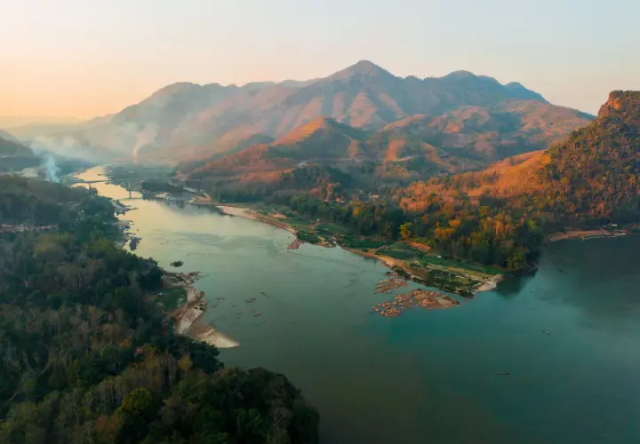 Sonnenuntergang über dem Mekong Delta. Berge, Wälder und ein breiter Fluss mit kleinen Booten.