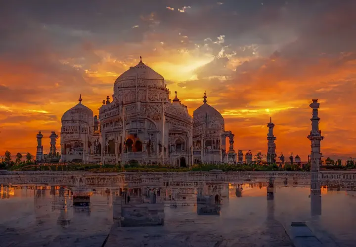 Das Taj Mahal spiegelt sich im Wasser, während ein dramatischer Sonnenuntergang den Himmel in leuchtenden Orange- und Rottönen färbt.