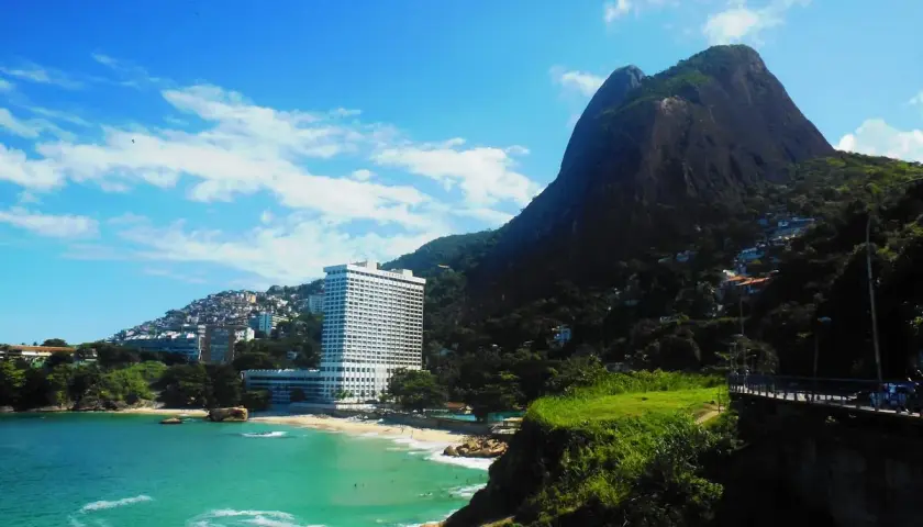 Traumhafter Blick auf Leblon, Rio de Janeiro: Türkisfarbenes Meer, ein Strand mit Palmen und das imposante Sheraton Hotel vor einem Berg.